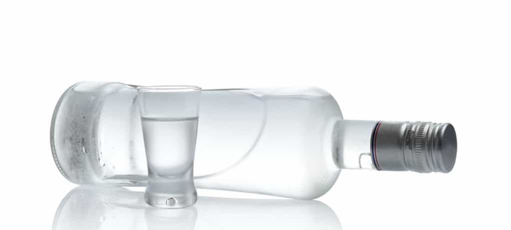 Close-up view of bottle lying on a table and glass of vodka next to it