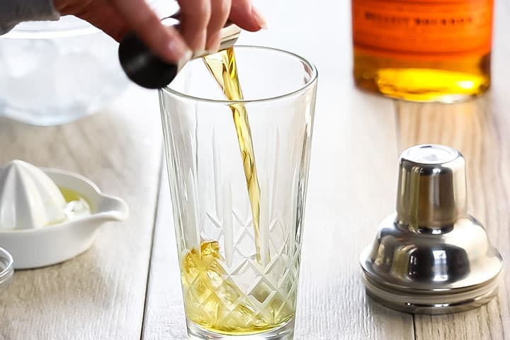whiskey being poured into a cocktail shaker.