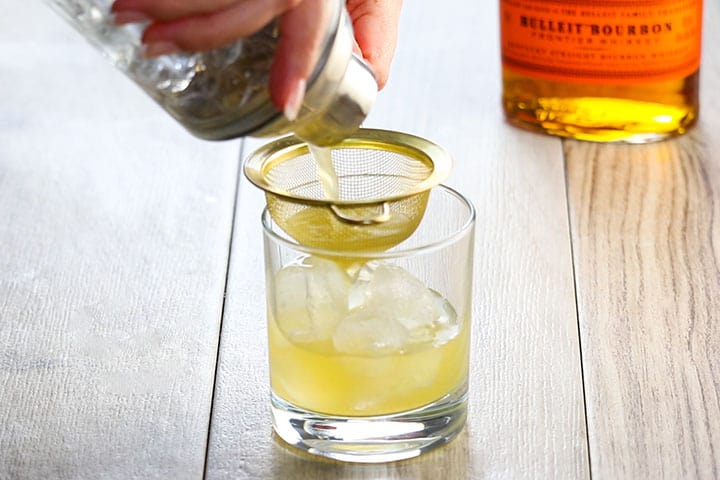 a Homemade Whisky sour being oured through a strainer into a coaktail glass