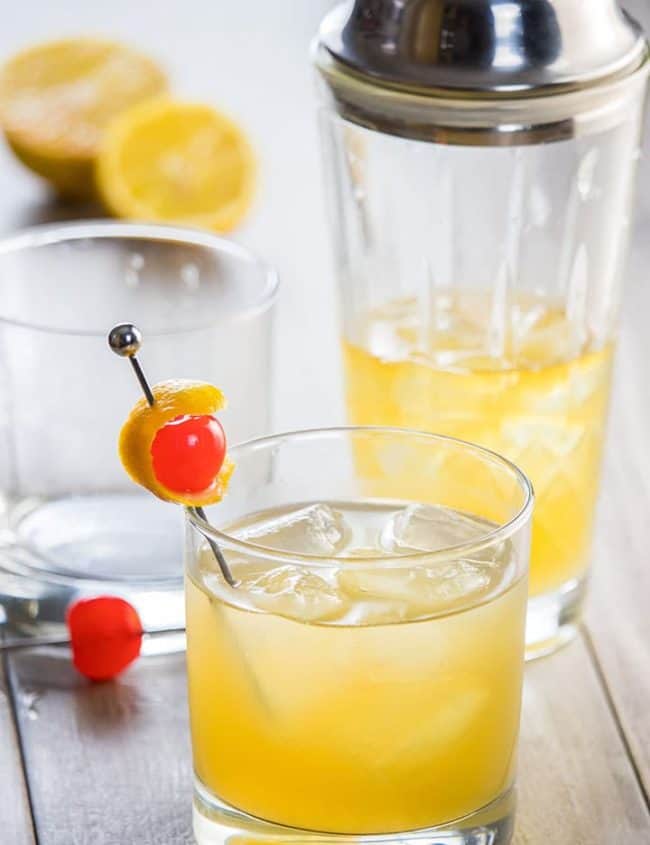 Homemade Whisky sour in a glass with ice and garnished with lemon peel and cherry