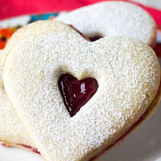 two Raspberry Butter Cookies on a plate dusted with powdered sugar