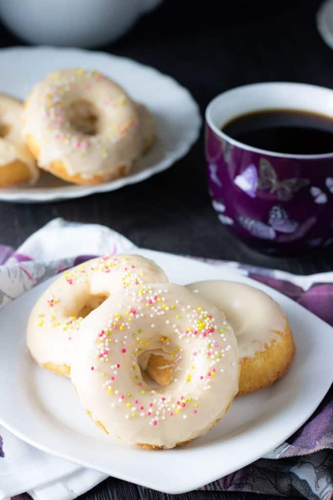 three Baked Vanilla Donuts on a plate with a cup of coffee behind it