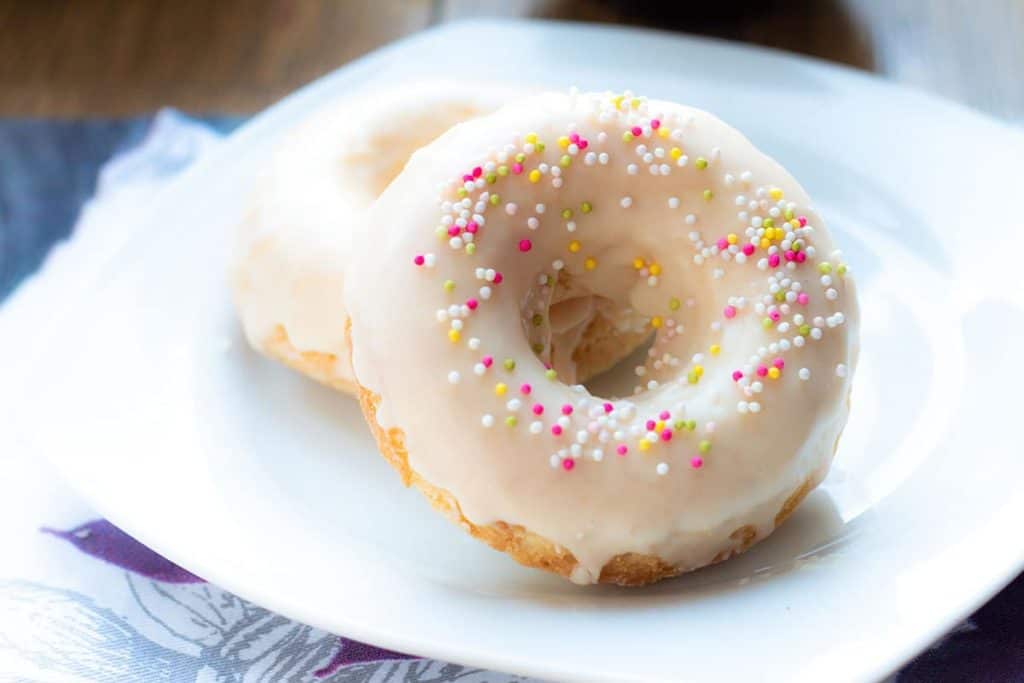 two Baked Vanilla Donuts on a plate with a cup of coffee behind it