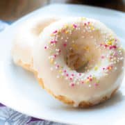 two Baked Vanilla Donuts on a plate with a cup of coffee behind it