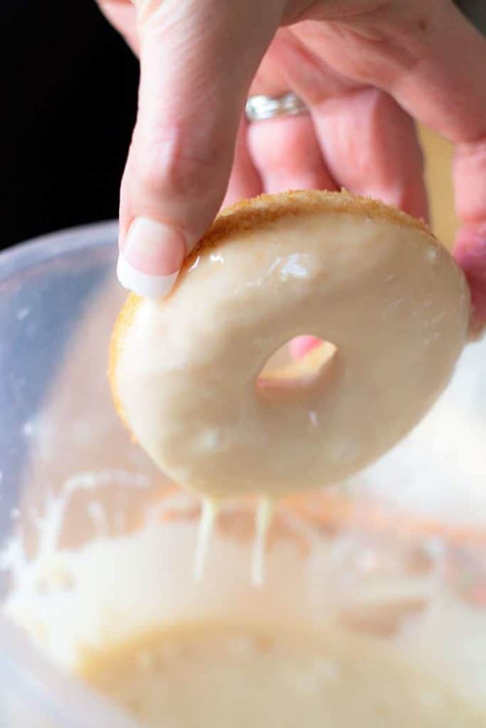 a Baked Vanilla Donut being dipped into the icing