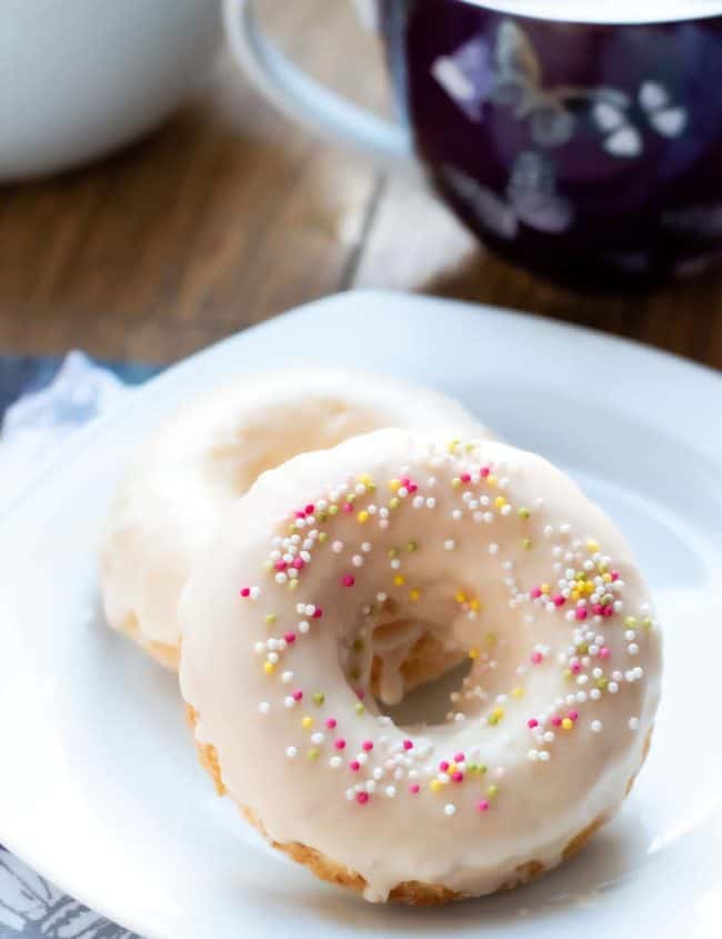 two Baked Vanilla Donuts on a plate with a cup of coffee behind it