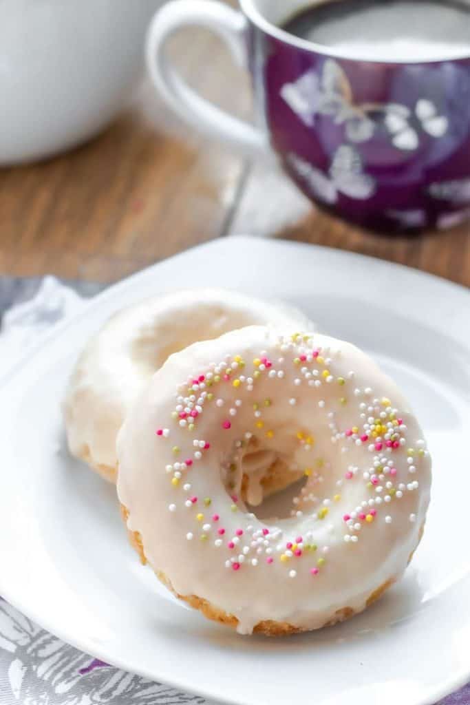 two Baked Vanilla Donuts on a plate with a cup of coffee behind it