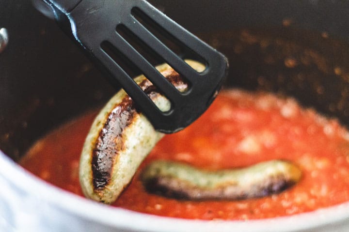 Sausage being added to the pot with the sauce