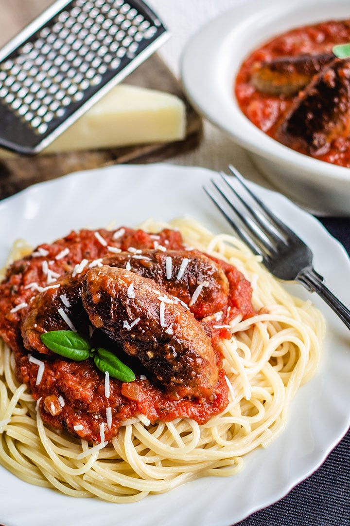 Spaghetti and Italian Sausage on a plate with cheese and a dish of sauce in the background