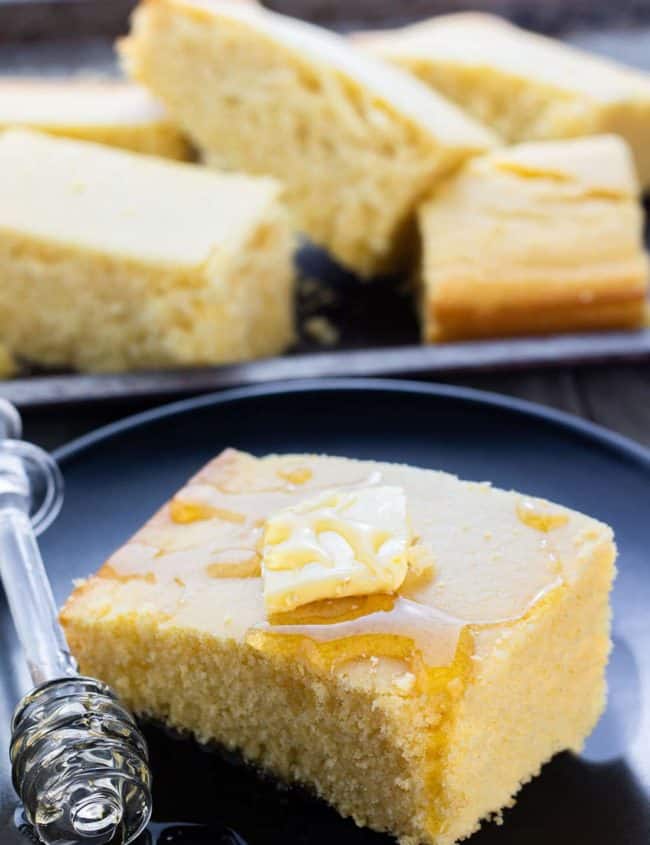 A piece of Cornbread on a plate topped with butter and drizzled with honey