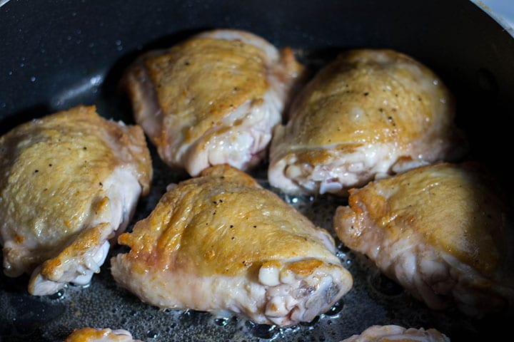 chicken thighs with browned skin cooking in the pan