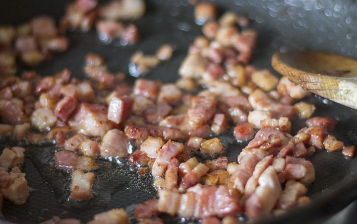 pancetta cooking in a pan with a wooden spoon