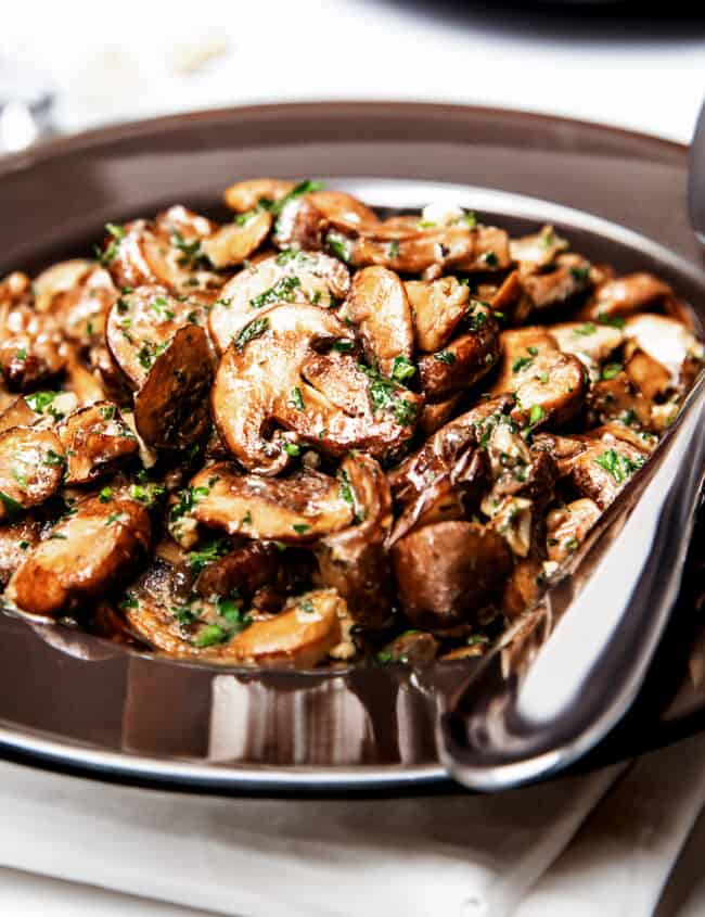 golden sautéed Mushrooms in a bowl with a serving spoon.