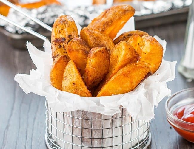 Seasoned Baked Potato Wedges in a metal serving basket sprinkled with salt