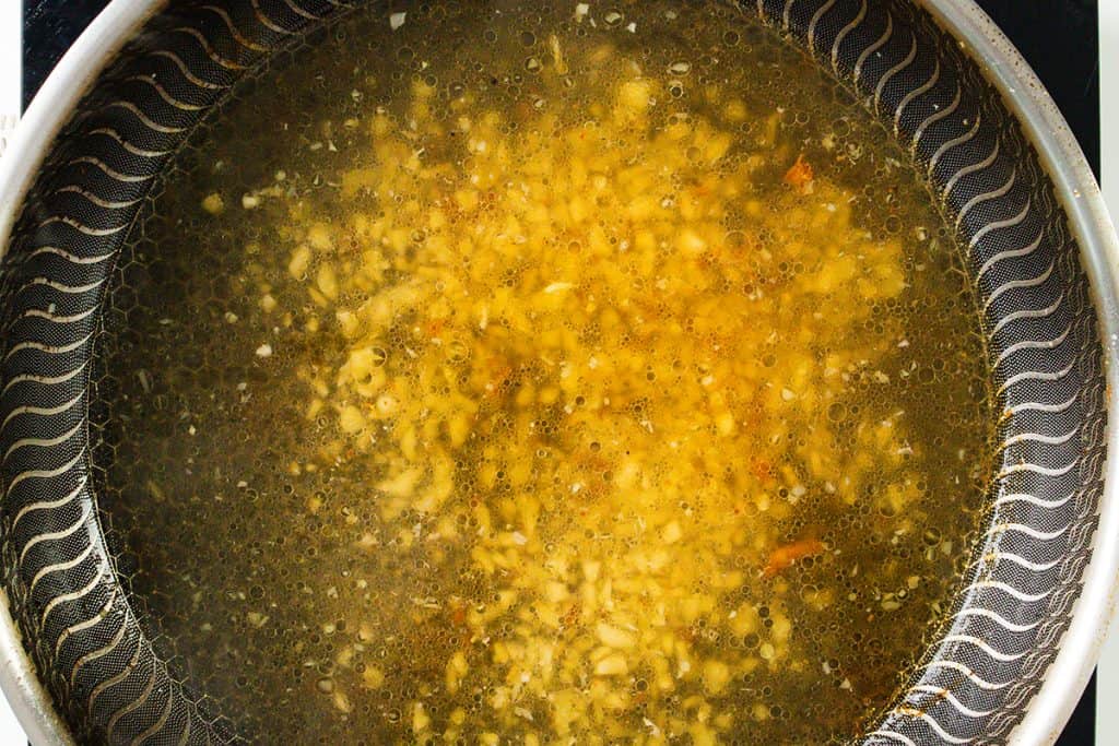 A close-up of chopped onions being saut&eacute;ed in oil in a pot, with bubbles forming around the golden pieces&mdash;an essential first step for flavorful dishes like Baked Garlic Chicken Thighs.