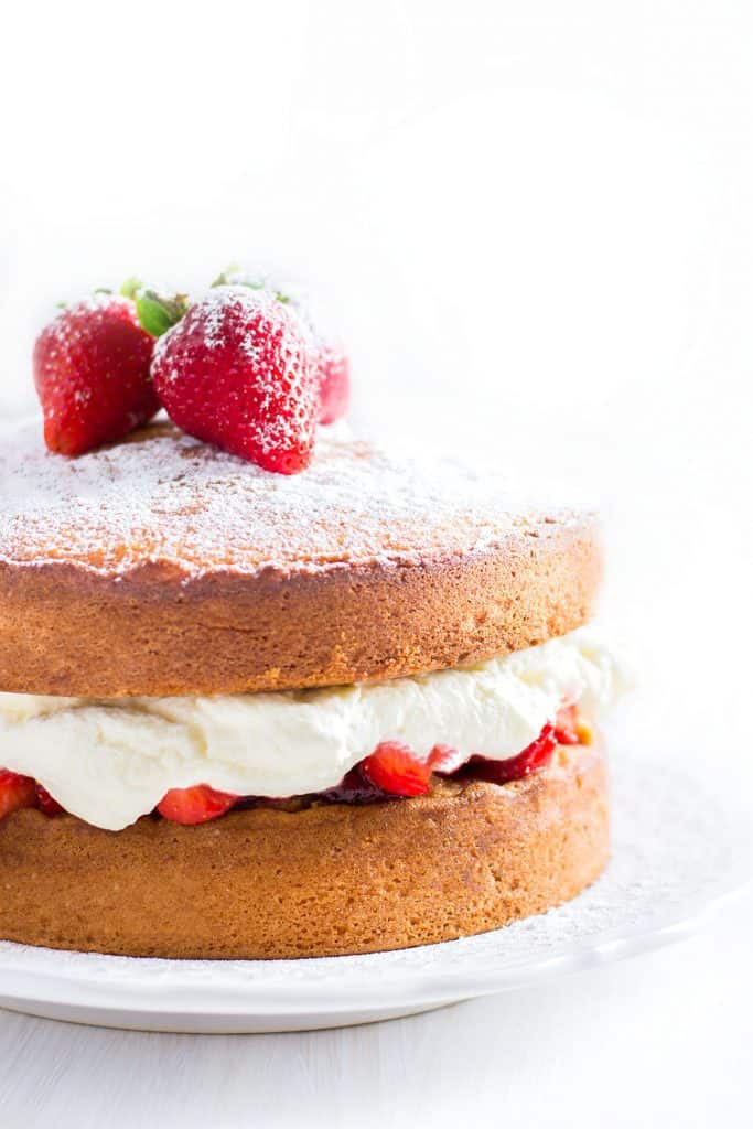 Lemon Sponge Cake filled with fresh strawberries and whipped cream topped with powdered sugar and three strawberries