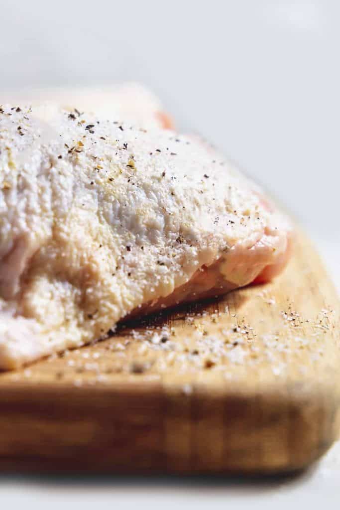 a chicken thigh on a cutting board seasoned with salt and pepper