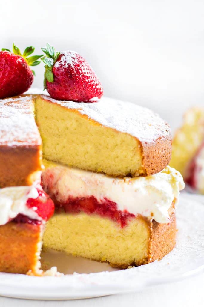 Lemon Sponge Cake filled with whipped cream and strawberries with a slice cut out