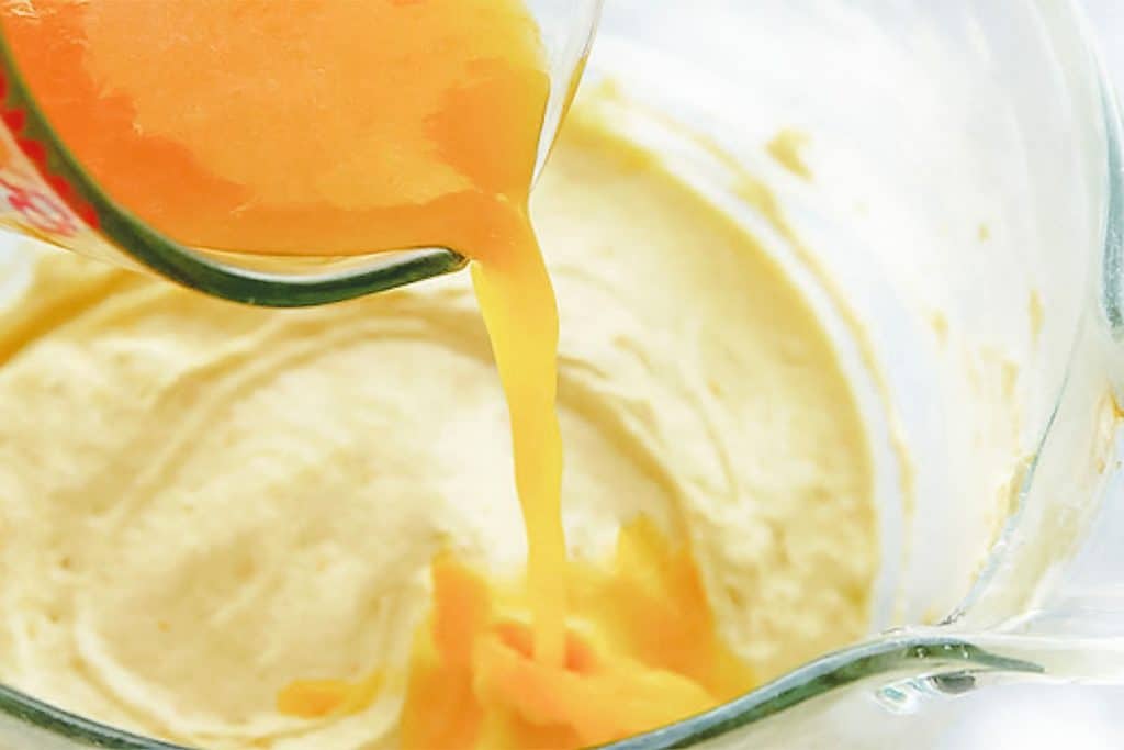 orange juice being poured into the cake batter mixture in the bowl