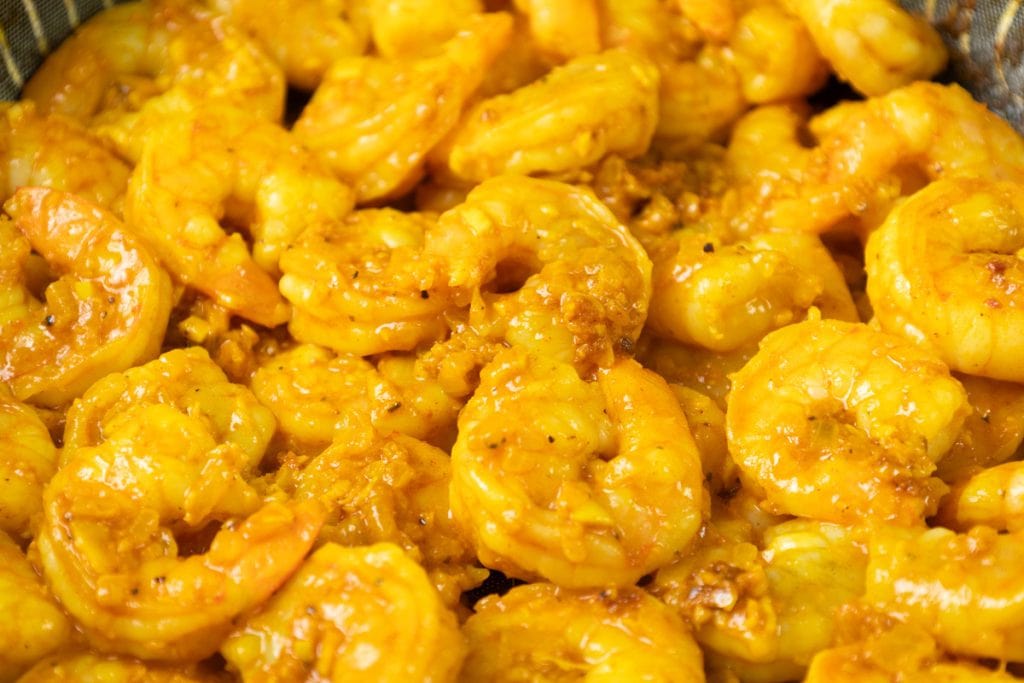 Close-up of cooked shrimp coated in a golden yellow sauce with visible spices and bits of garlic, capturing the rich flavors of Coconut Shrimp Curry.