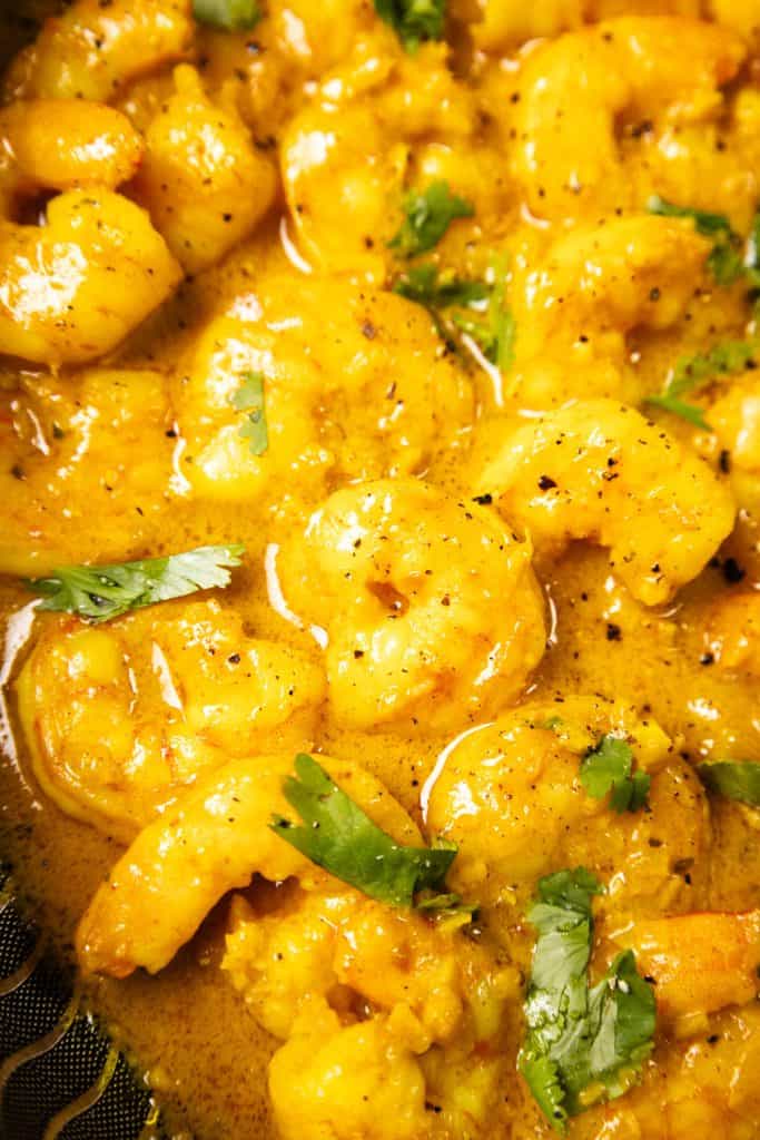 Close-up of Coconut Shrimp Curry cooked in a yellow curry sauce, garnished with chopped cilantro and black pepper.
