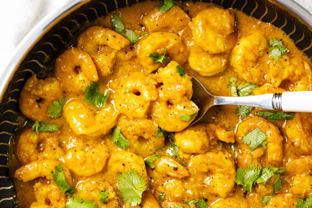 Coconut Shrimp Curry in a creamy orange sauce, garnished with fresh cilantro leaves, served in a bowl with a white-handled fork.