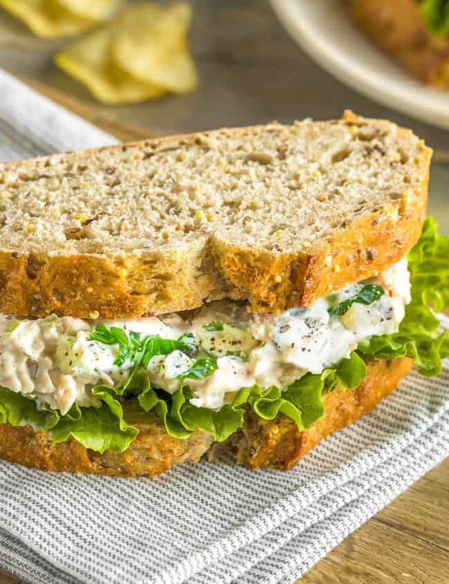 A tuna salad sandwich on a cutting board with potato chips in the background