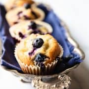 Five Blueberry muffins lined up on a silver tray with an ornate handle