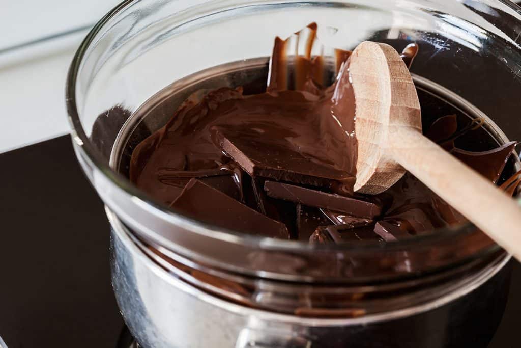 Melted chocolate being mixed with a wooden spoon over a double boiler
