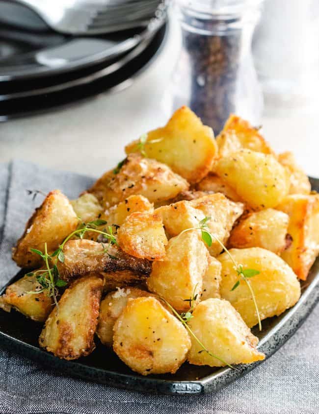 golden roasted potatoes piled high on a dish sprinkled with salt and fresh thyme