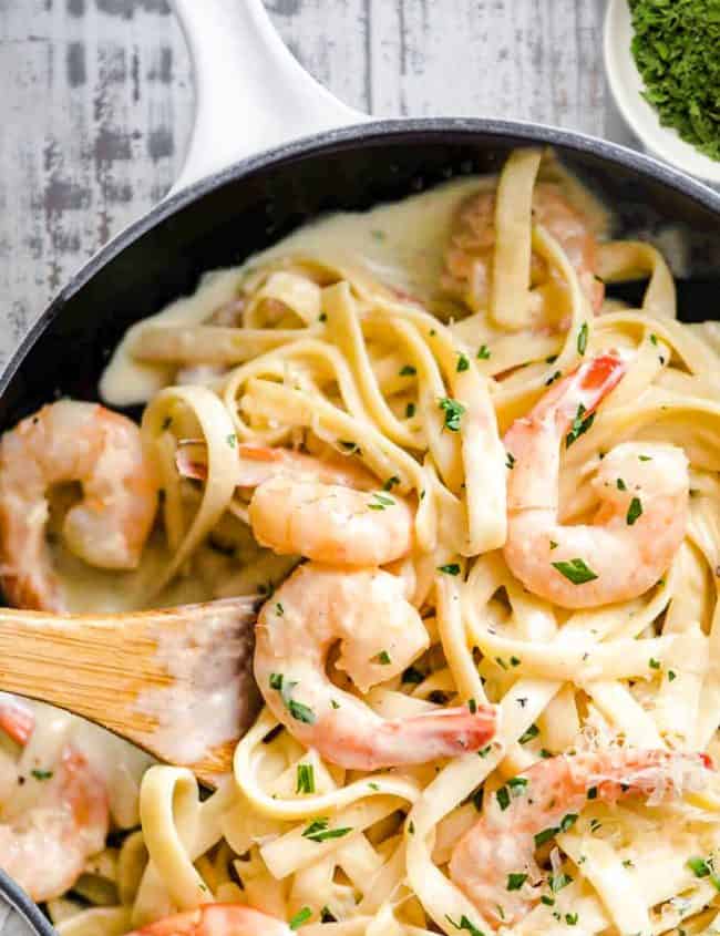 a pan of Fettuccine Alfredo with shrimp and garnished with parsley