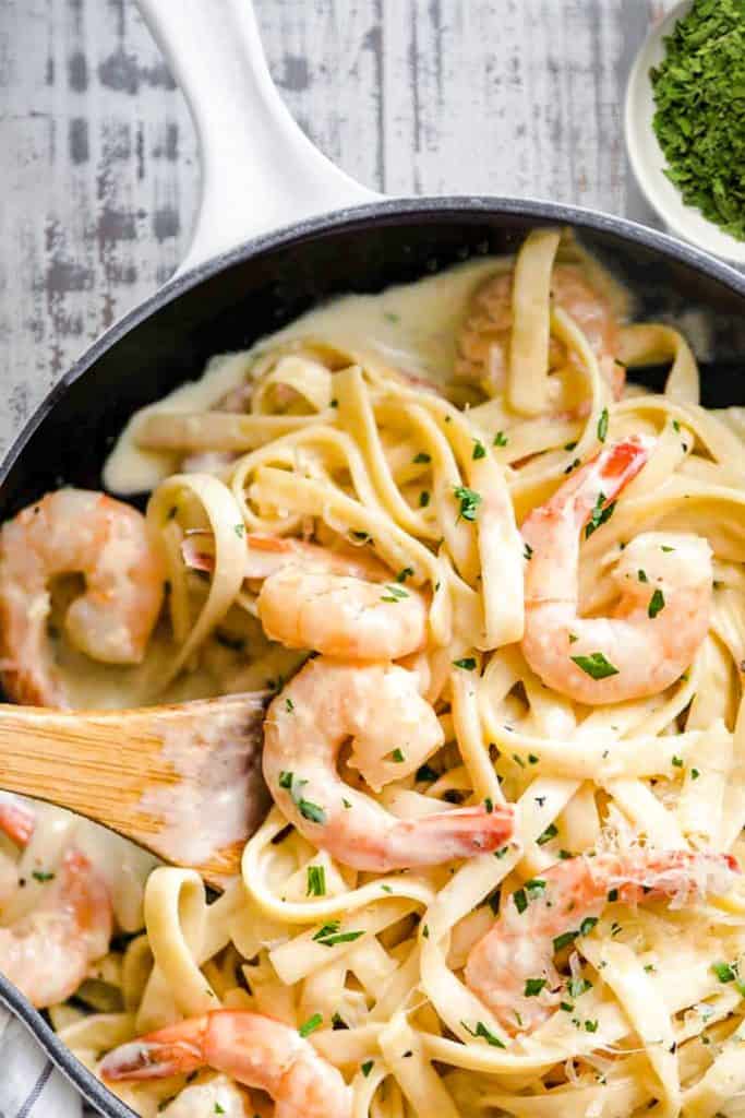 a pan of Fettuccine Alfredo with shrimp and garnished with parsley