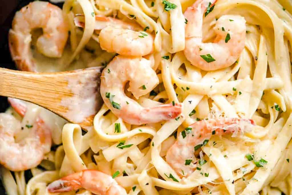 a pan of Fettuccine Alfredo with shrimp and garnished with parsley