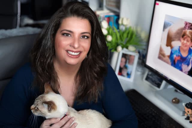 Erren sitting at her desk with her cat in her lap, smiling at the camera