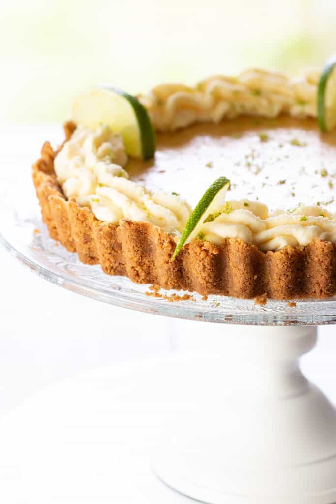 A key lime pie swirled with whipped cream around the edge and garnished with lime slices and zest.