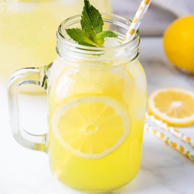 a glass of fresh squeezed lemonade with a straw and lemon slices and fresh mint as garnish
