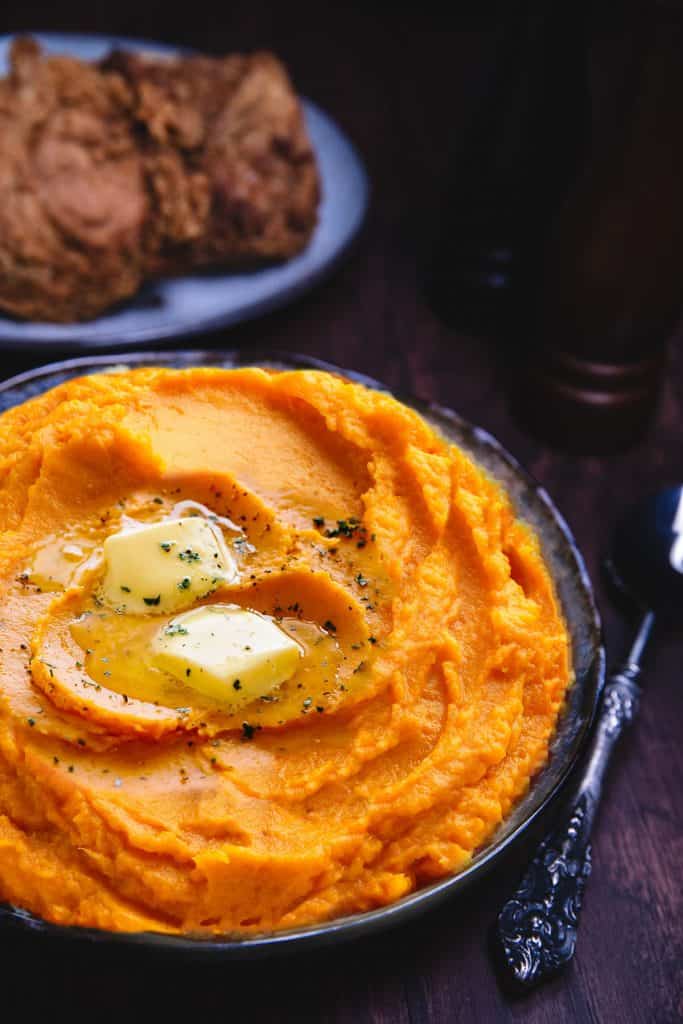 a dish of mashed sweetpotatoes topped with butter and ground black pepper