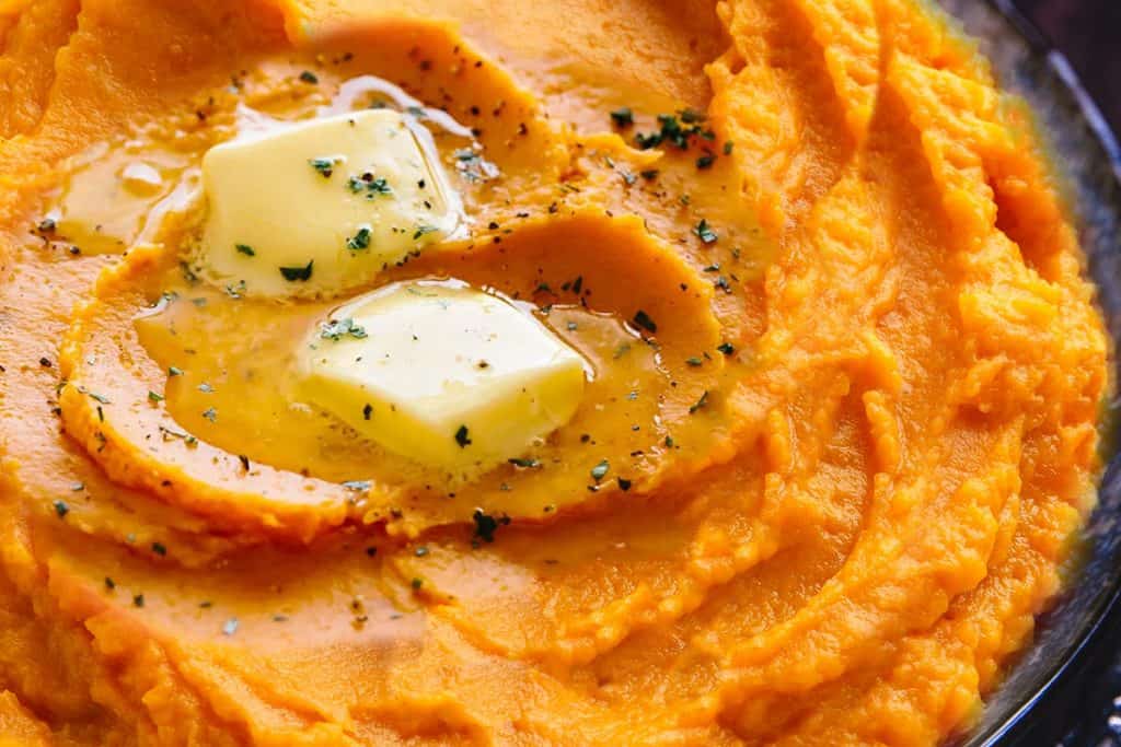 A close up of mashed sweet potatoes topped with butter and ground black pepper