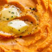 a dish of mashed sweetpotatoes topped with butter and ground black pepper