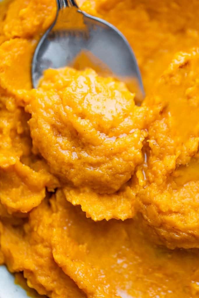 A spoon running through mashed sweet potatoes