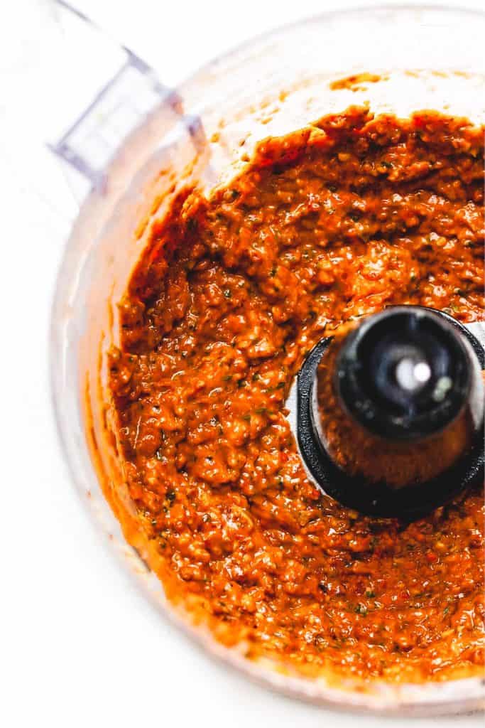 a food processor bowl with the blended red pesto sauce.