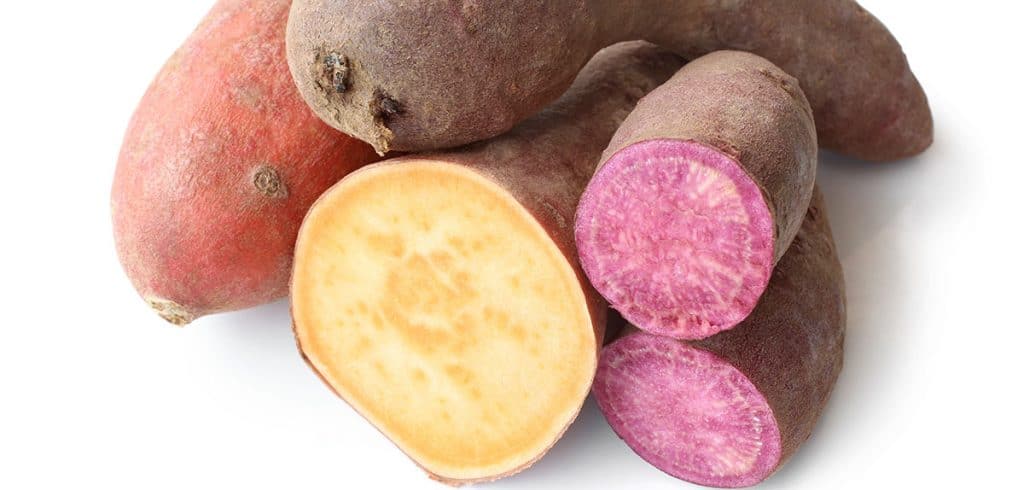 different types of sweet potatoes in a pile with some cut open to show purple and orange colors