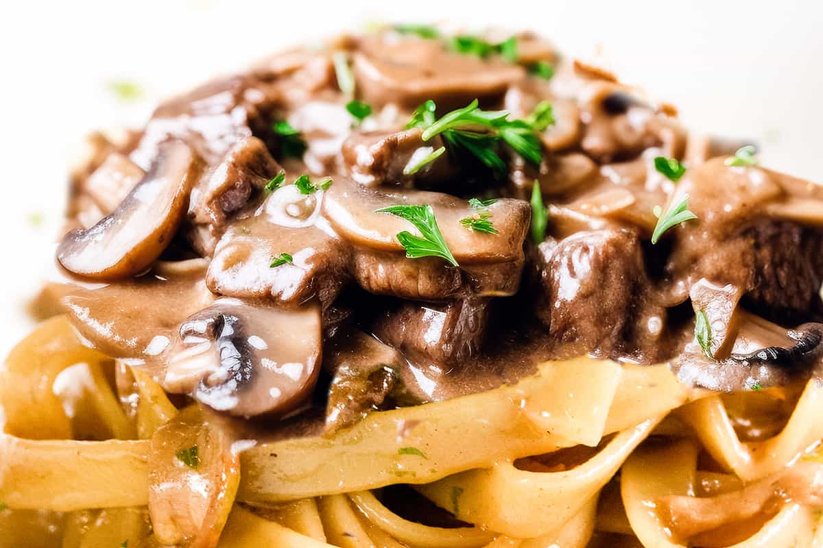 a close up image of Beef and mushrooms in a creamy Stroganoff sauce over noodles