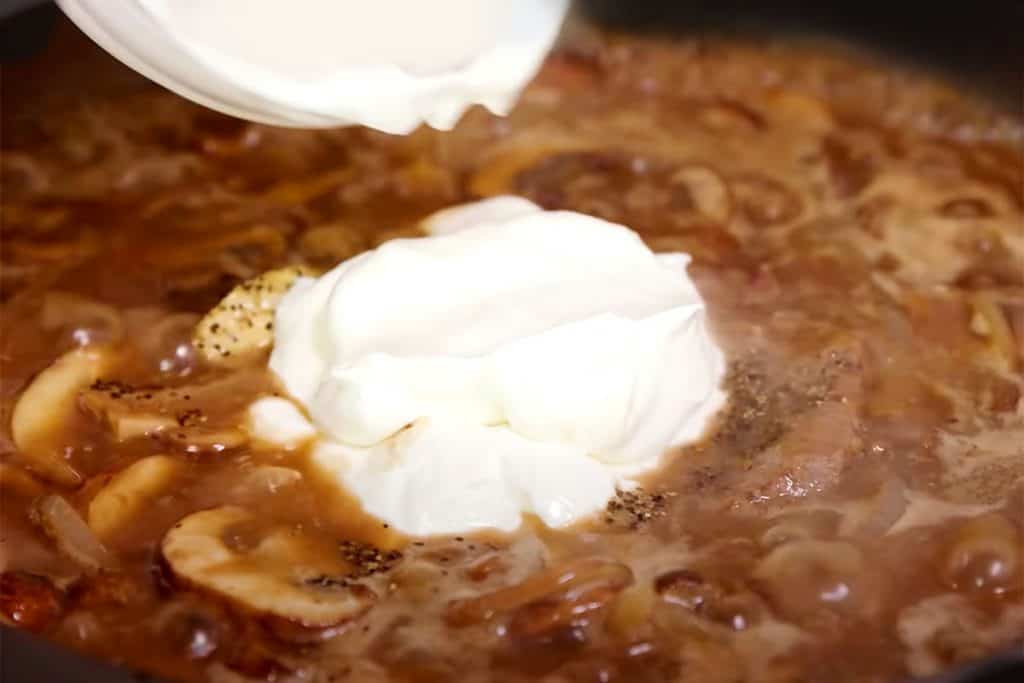 sour cream being added to the pan with the sauce