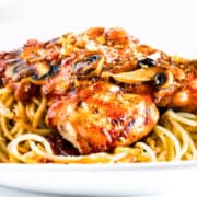 a close up image of Chicken Cacciatore on spaghetti with a glass of red wine in the background.