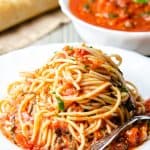 A plate of pasta with marinara sauce with a fork next to it and fresh basil near the dish