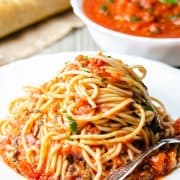 A plate of pasta with marinara sauce with a fork next to it and fresh basil near the dish