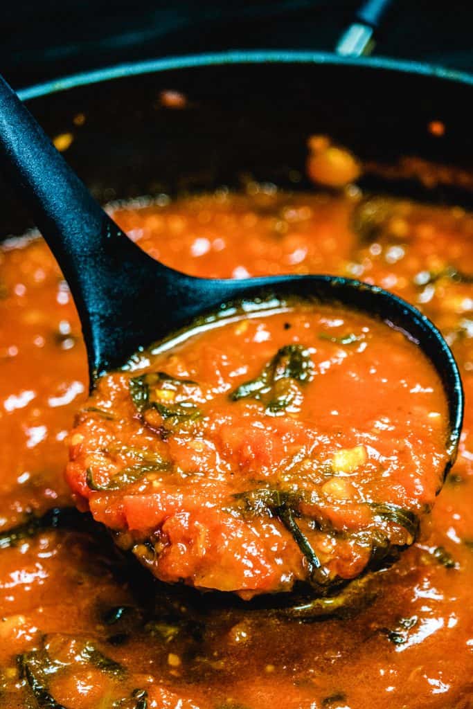 a spoon soppong up tomato sauce from a pot