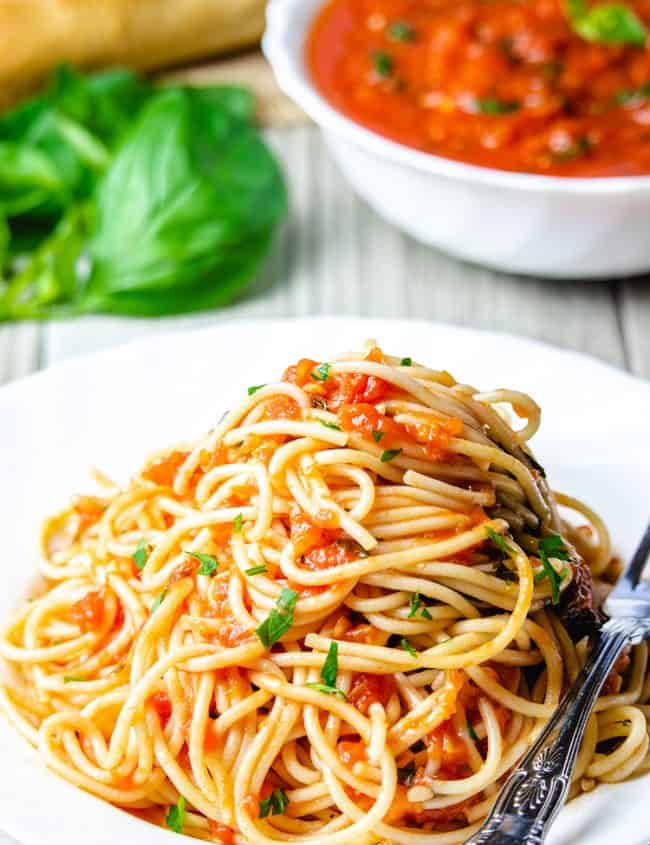A plate of pasta with marinara sauce with a fork next to it and fresh basil near the dish