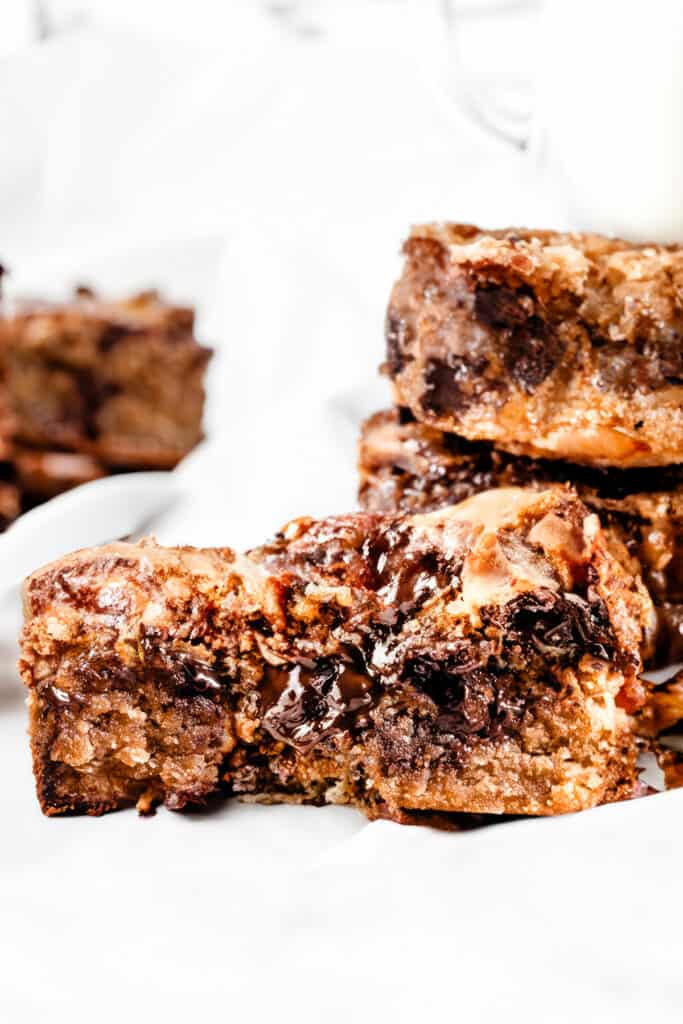 a close up image of a chocolate chip blondie with a gooey center exposed and more chocolate chip blondies in the background.